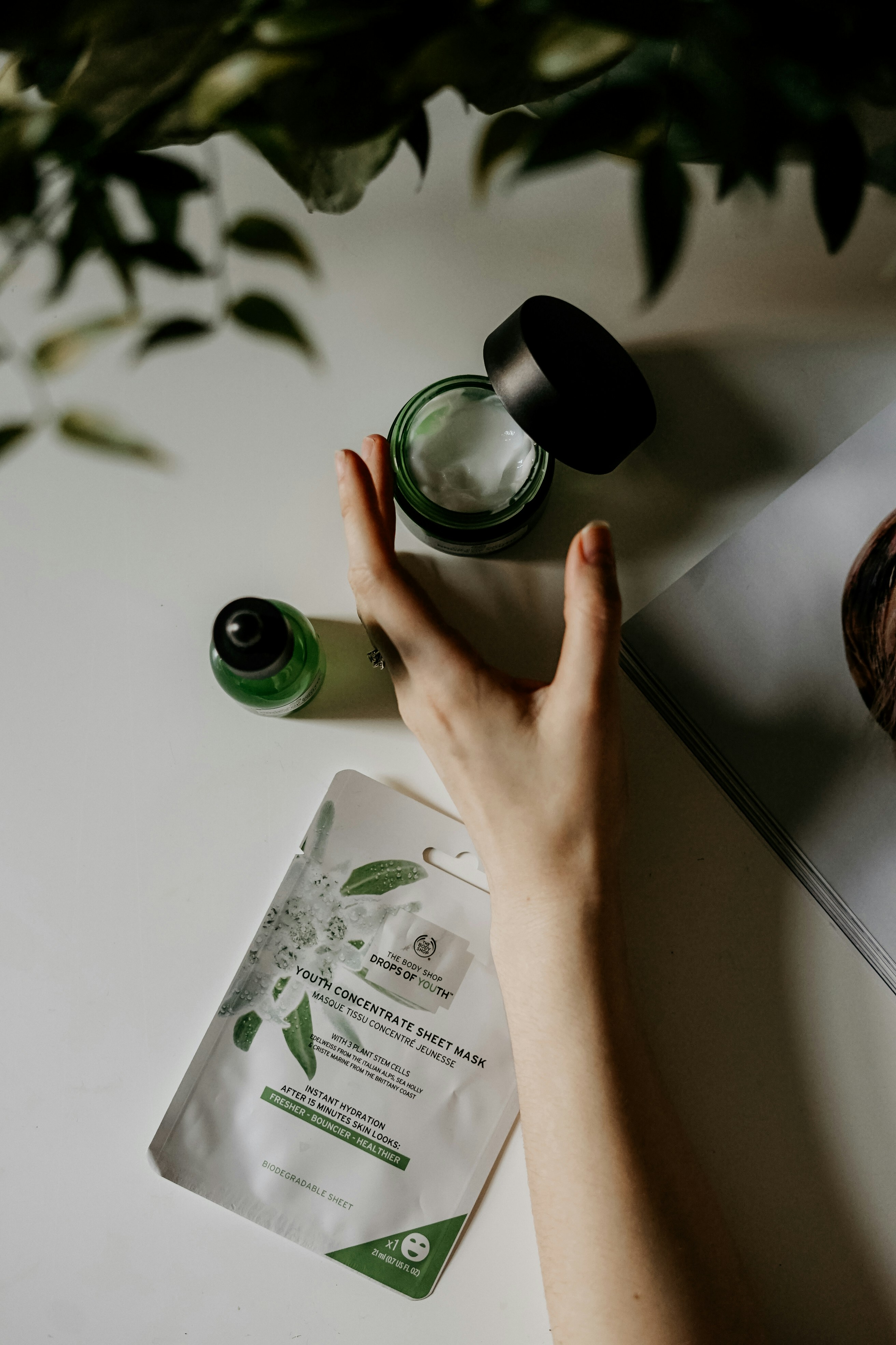 A hand holding skincare cream beside a sheet mask